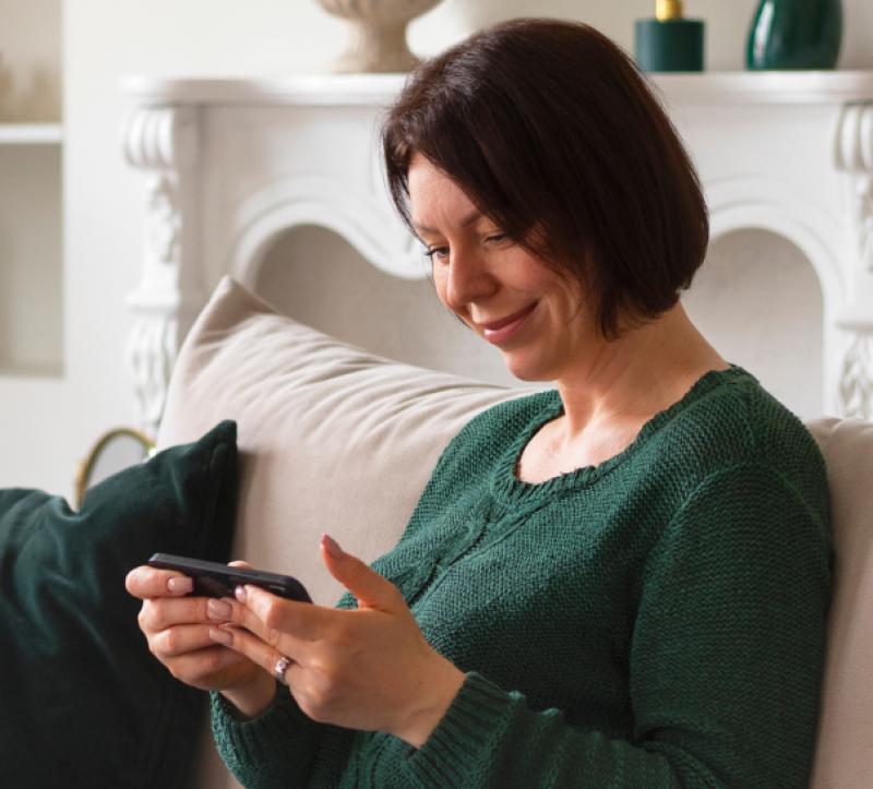 A woman sat on a sofa looking at her mobile phone